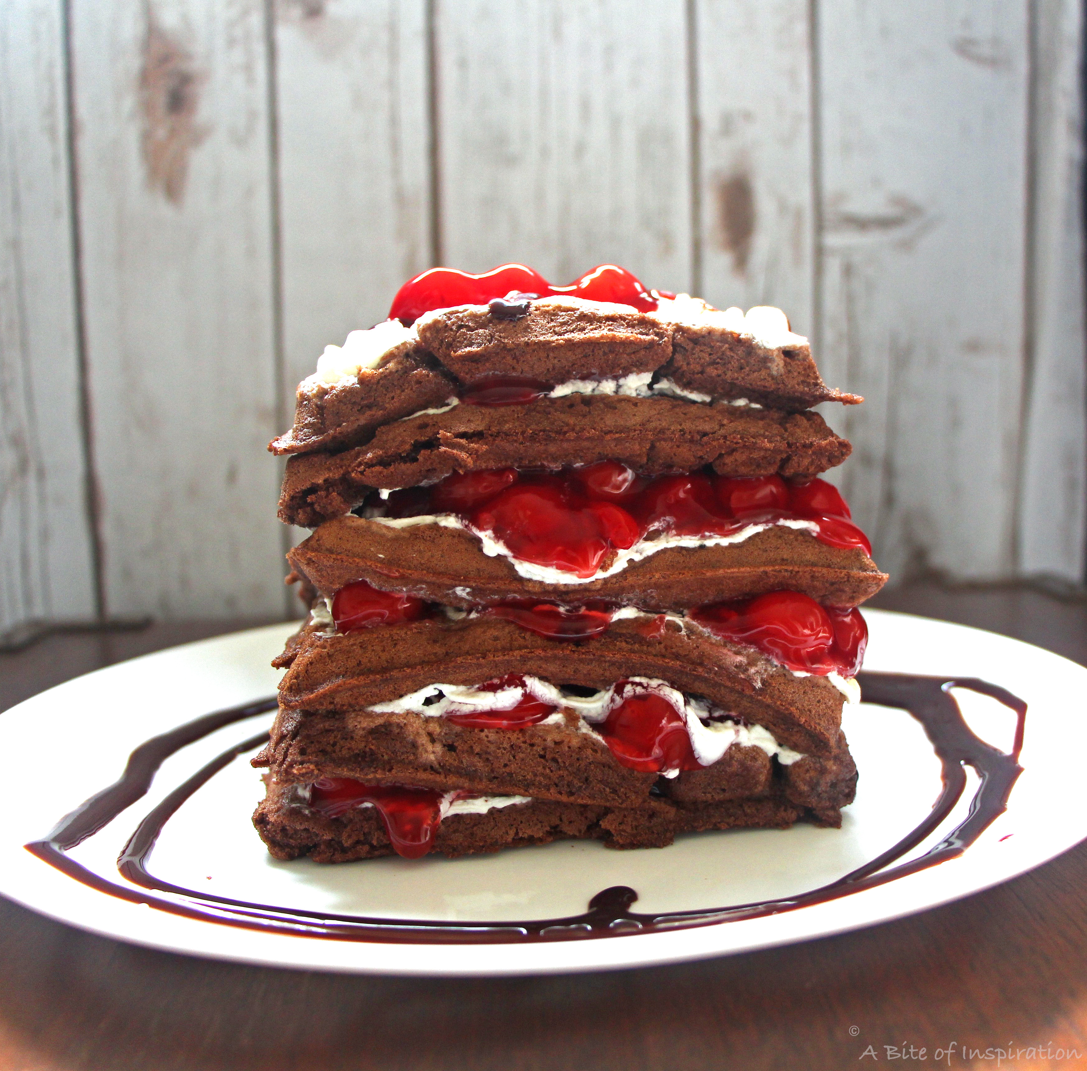 Chocolate cake waffles stacked high with whipped cream and cherries