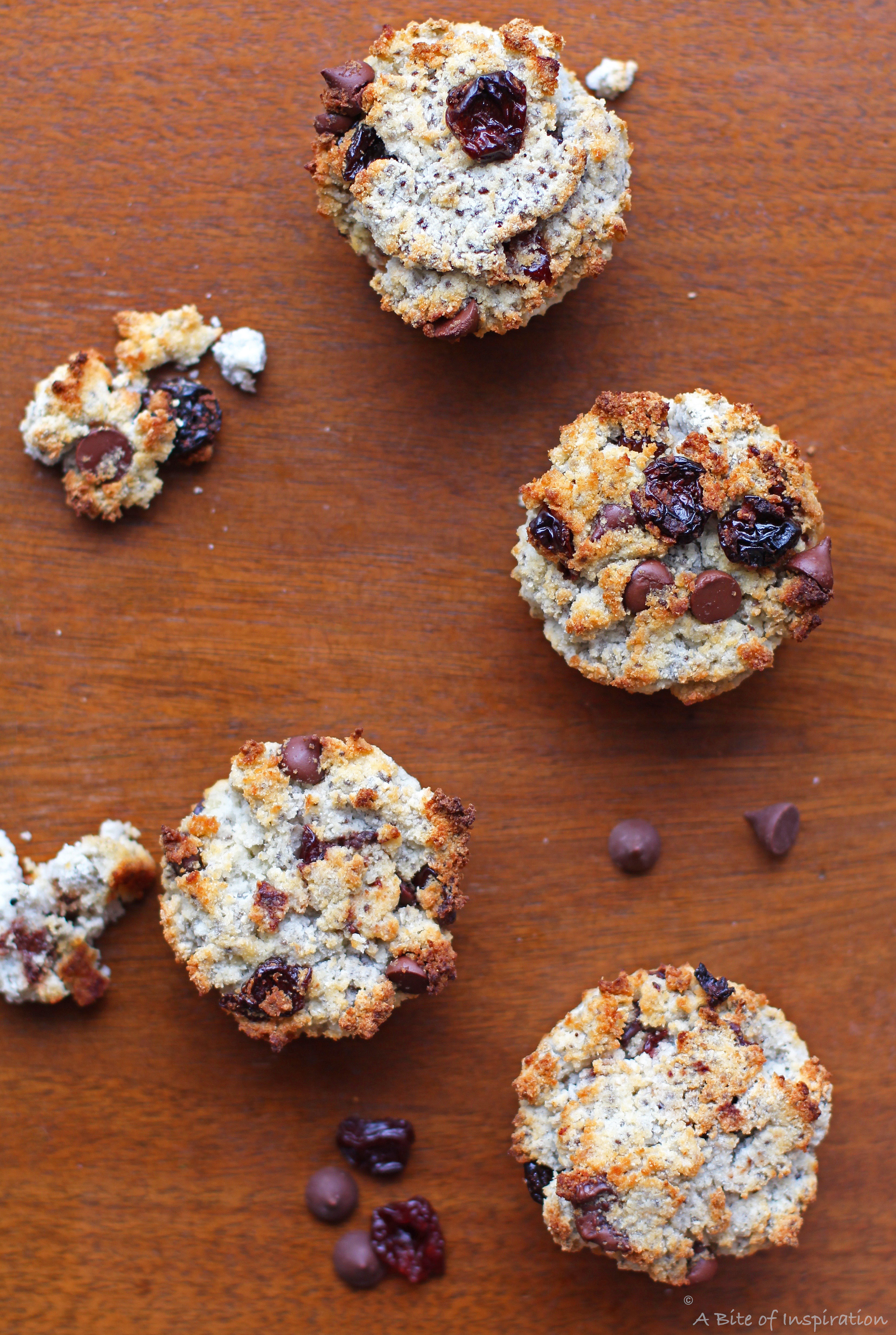 Several muffins scattered on a table surrounded by chocolate chips, cherries, and muffin crumbs