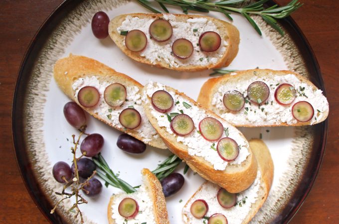 Plate of Soft Cheese Crostini with Pickled Grapes and Rosemary with grapes and sprigs of rosemary around the sides