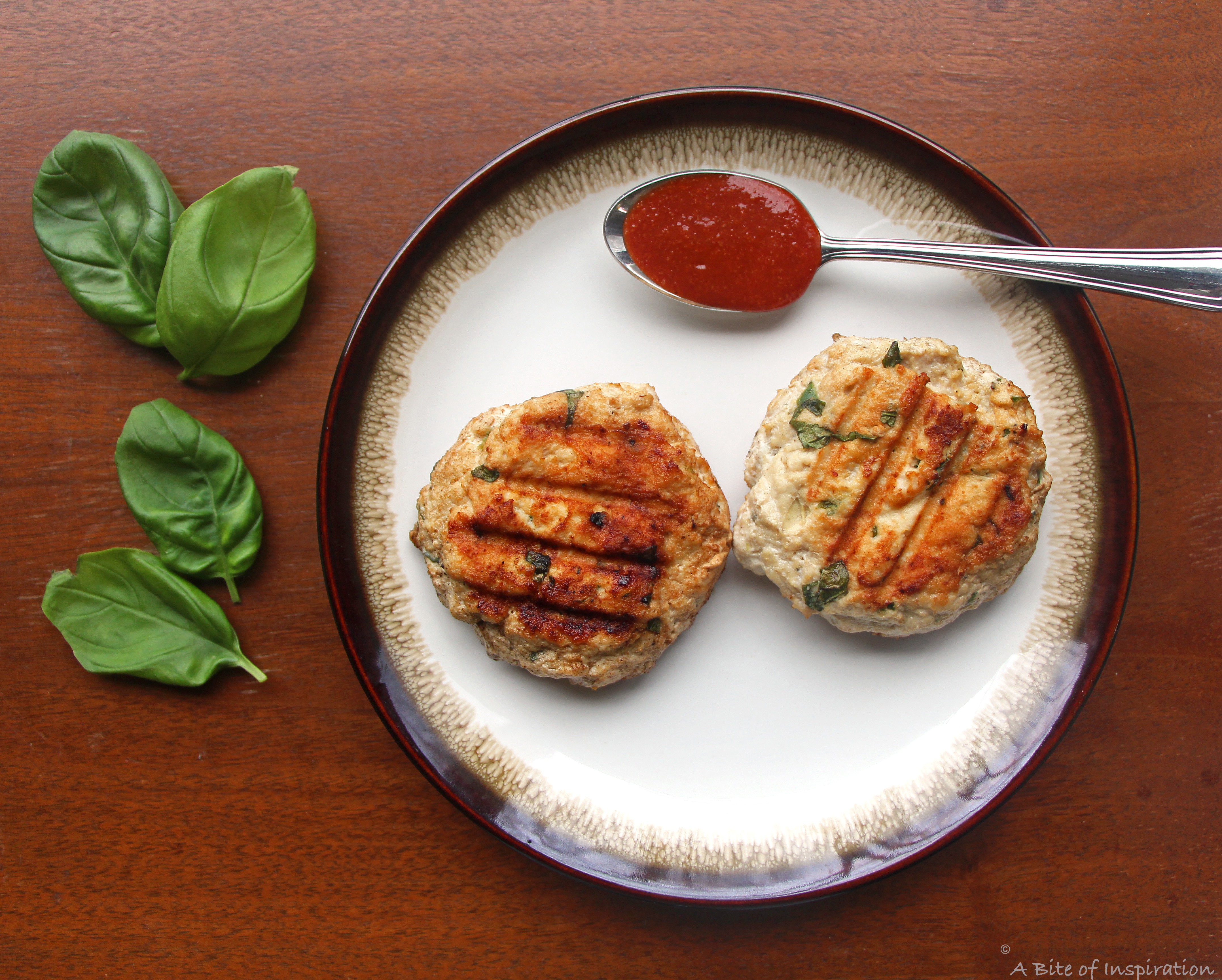 Two Thai-Style Chicken Burgers without buns, with Sriracha and basil on the side 