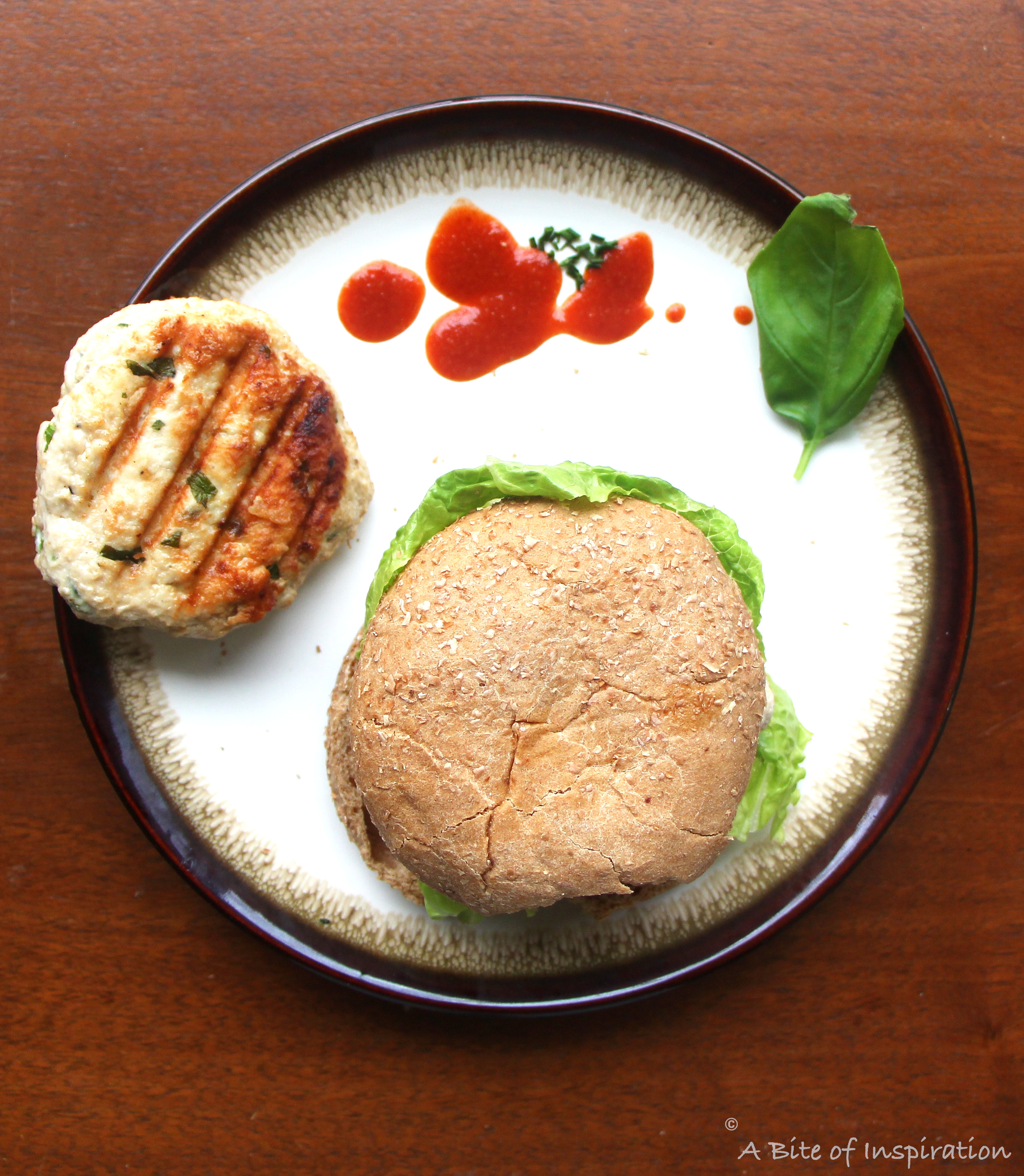 Thai-Style Chicken Burger with Sriracha Mayo on a plate with an extra burger patty and sriracha on the side 